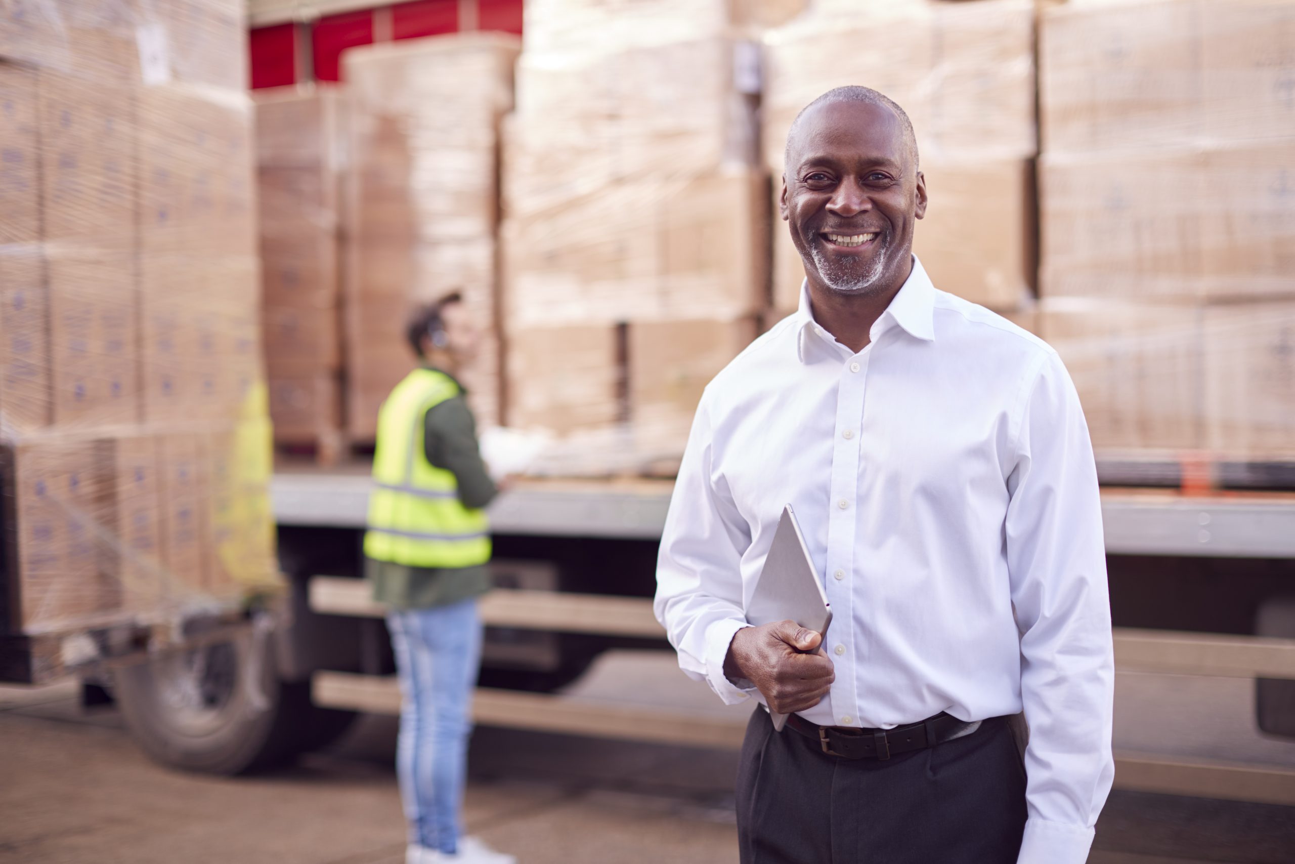 man smiling, holding a tablet, worker in the background